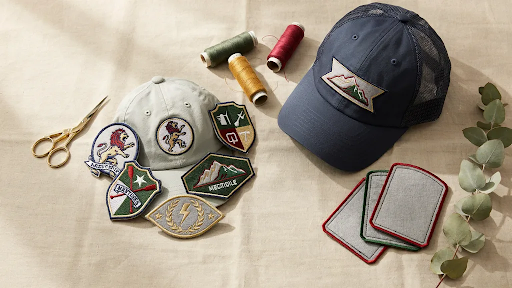 A cap on a white cloth backdrop with several rolls of threads and patches besides it