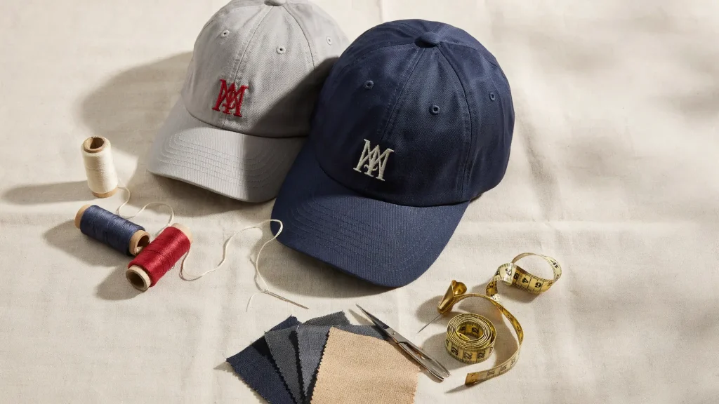Two embroidered baseball caps are displayed with colorful spools of thread, fabric swatches, scissors, and a measuring tape